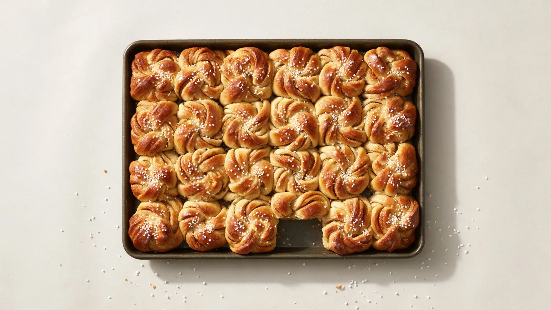 A baking tray of glossy cardamom buns with one missing.